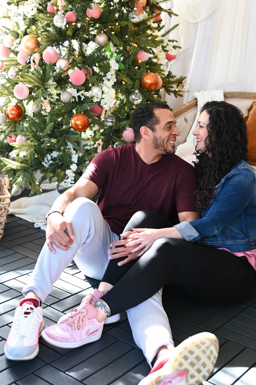 A couple sitting in front of a decorated Christmas tree, engaged in a moment of laughter and intimacy, reflecting a warm, festive spirit.