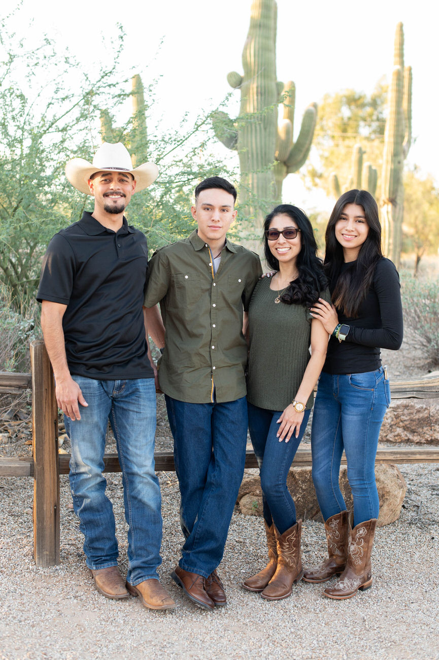 A family of four dressed in Western attire, standing confidently in a desert landscape with tall cacti and clear blue skies.