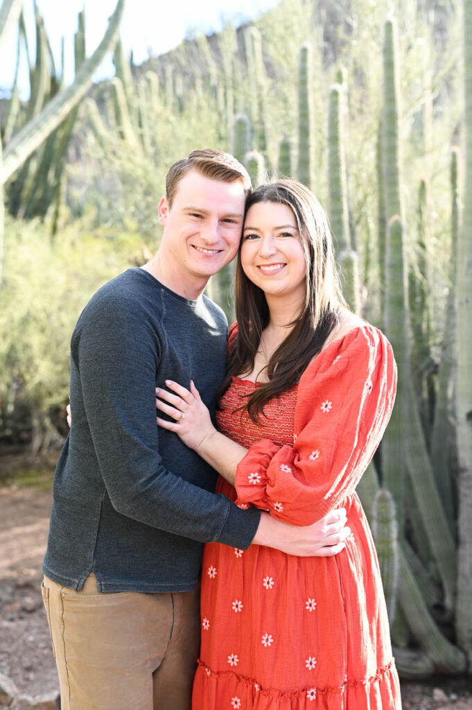 A couple in casual attire smiling and embracing in a cactus garden, with the Desert Botanical Garden in Arizona’s unique flora in the background